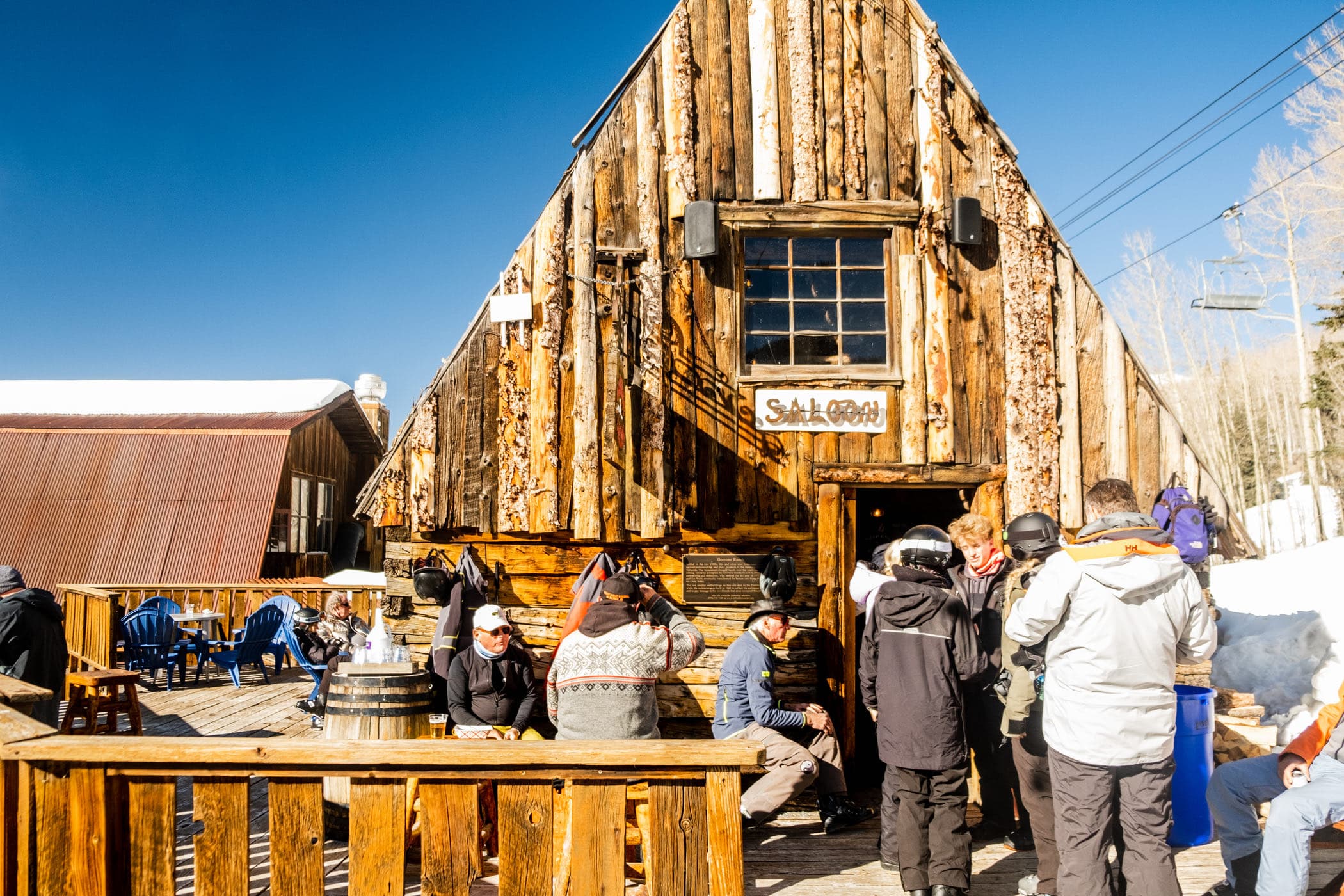 Skiers on the sunny deck outside the old timber saloon at Gorrono Ranch, mid-mountain.