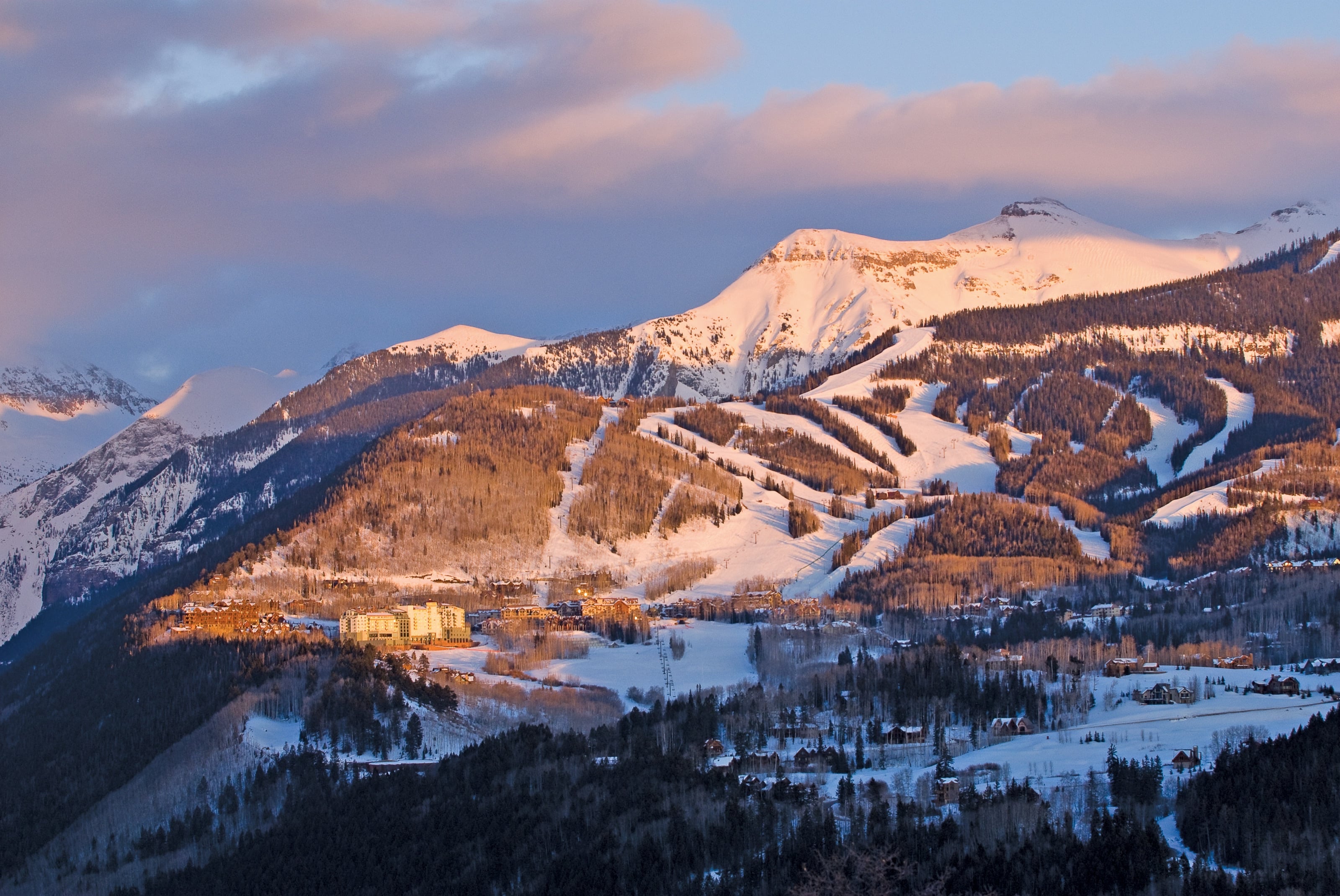 Mountain Village and the ski runs in alpenglow at dusk, snowy peaks behind.
