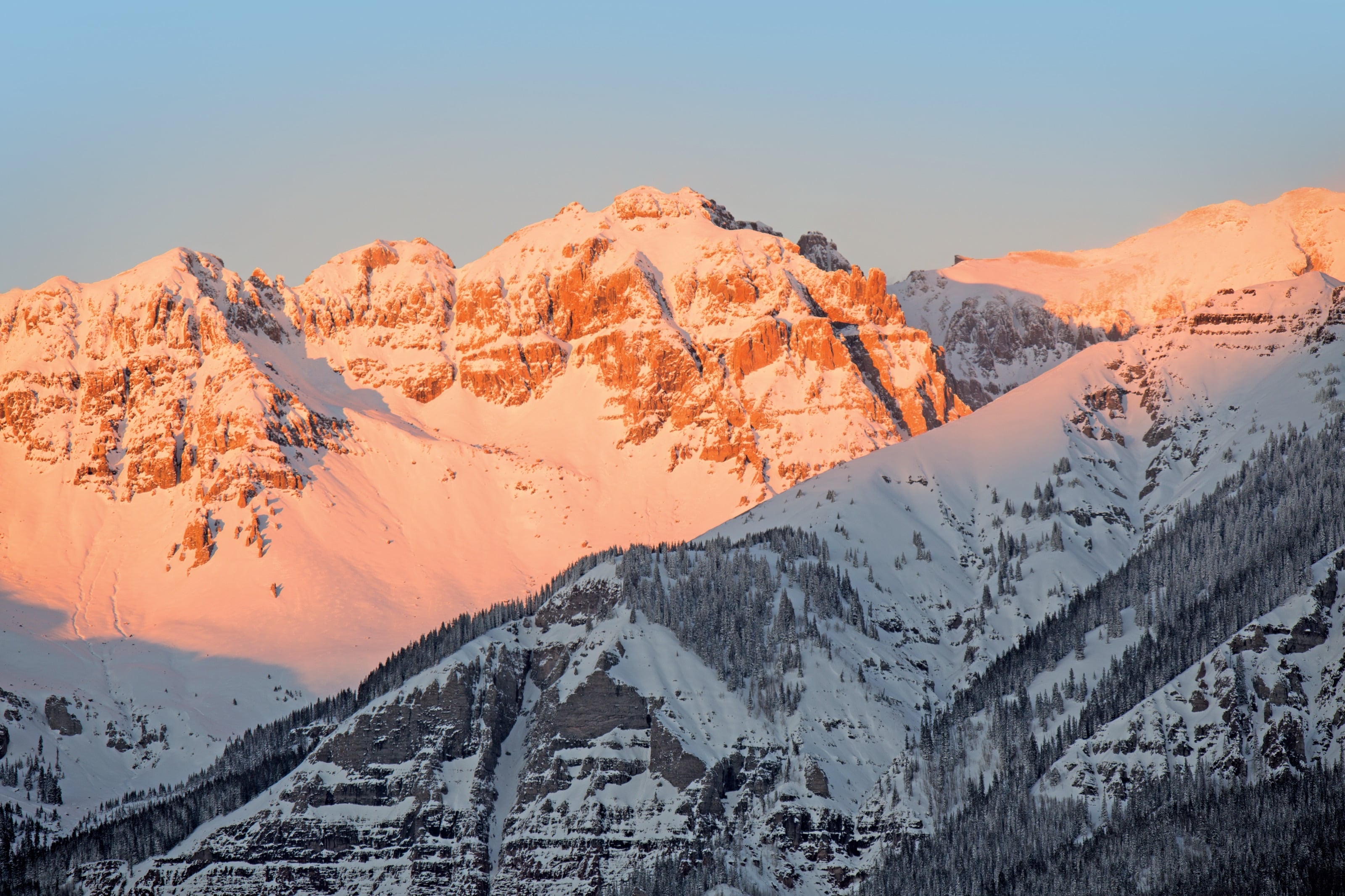 Sunset light turning the snowy San Juan peaks orange and pink above shadowed slopes.